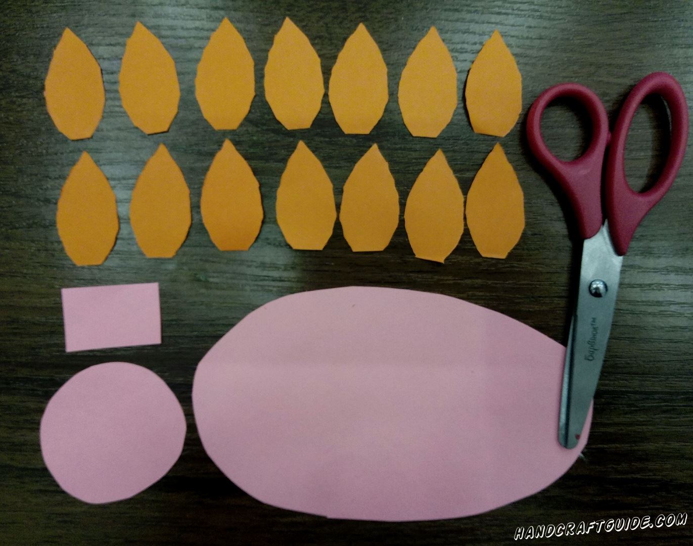 Для начала вырезаем все необходимые детальки. Берем оранжевую бумагу и вырезаем из нее 14 одинаковых листочка и один клювик. Затем берем розовый цвет и вырезаем большой овал, круг и маленький прямоугольник
