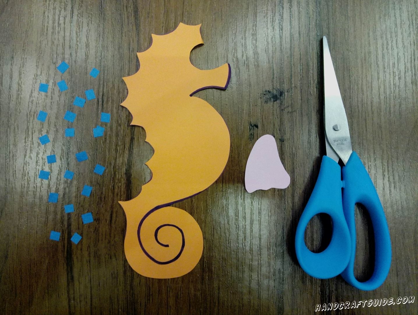 To begin with, we need to draw on the yellow sheet of paper, and then cut out the silhouette of the seahorse as in the photo. Then cut out a lot of small squares with blue paper and a fin of white