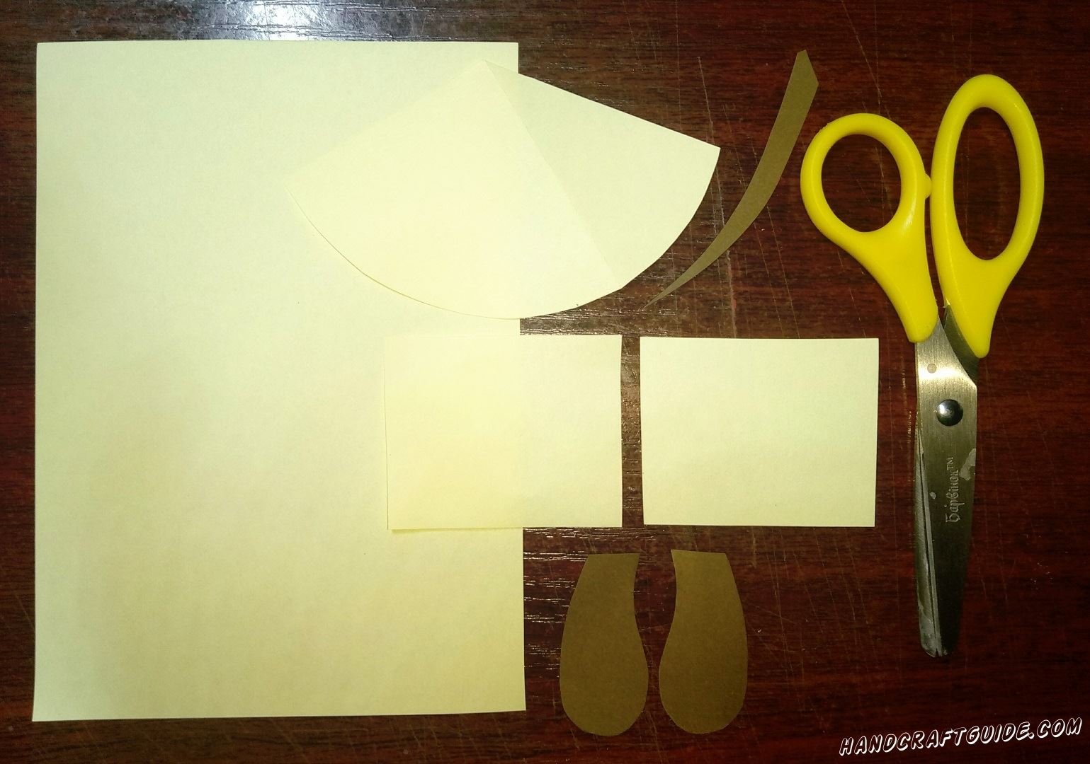 Из бумаги светло-жёлтого цвета мы вырезаем два одинаковых прямоугольника и треугольник с закругленной широкой стороной. Теперь берем коричневую бумагу и вырезаем два ушка и хвостик.