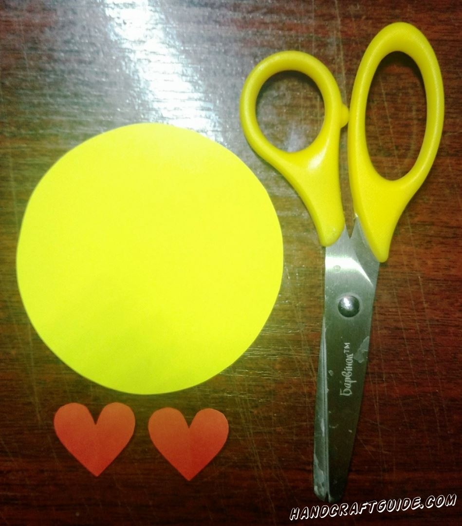 Вырежем желтый круг и два маленьких красных сердечка, из бумаги.