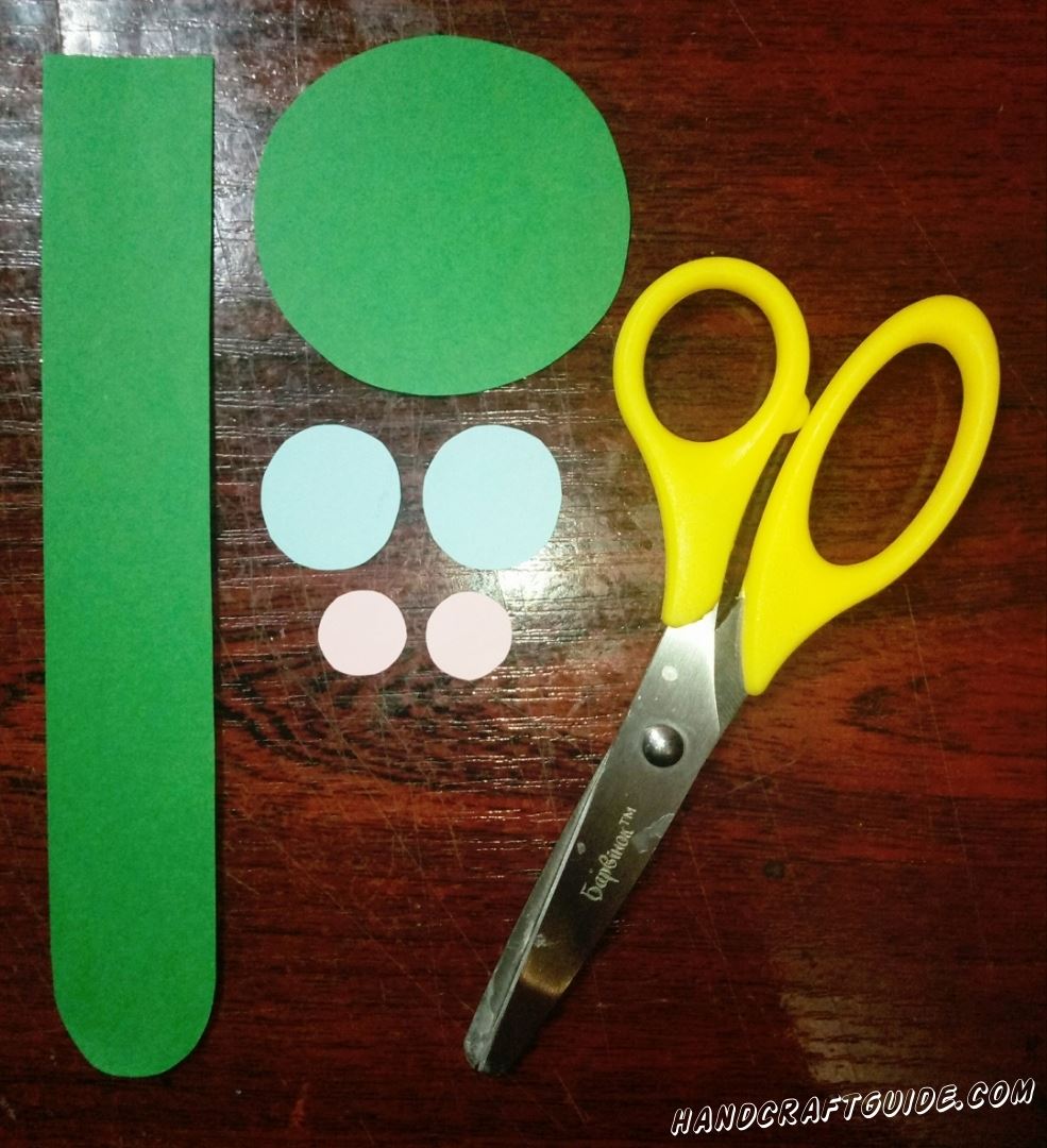 Для начала, вырезаем все необходимые нам бумажные фигурки:  полоску зелёного цвета, с закругленными углами с одной стороны, зелёный круг, два небольших голубых кружка и два светло-розовых ещё меньшего размера.